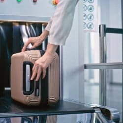 A person places their luggage on the conveyor belt of a TSA bag scanner.